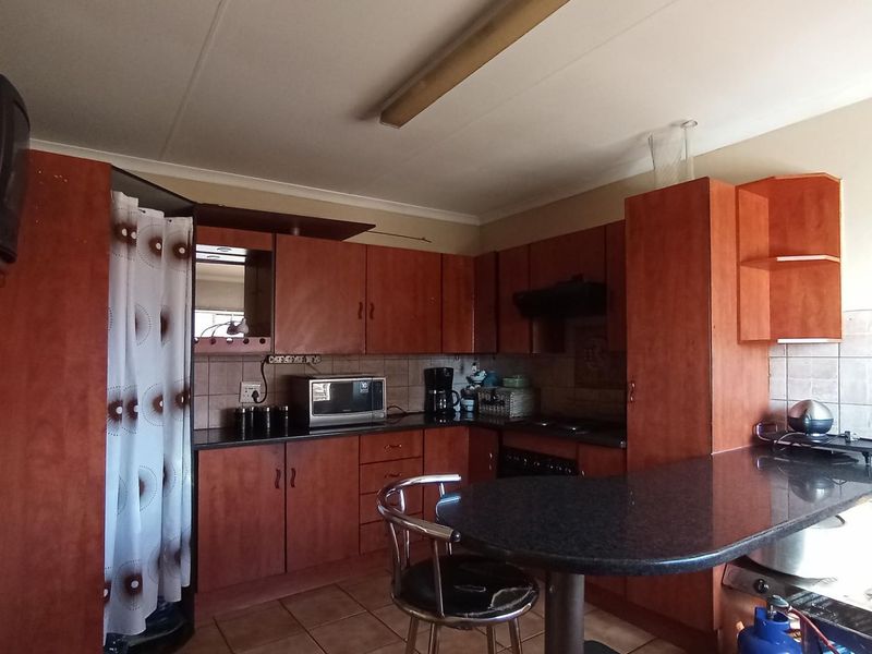 A functional kitchen featuring wood-look cabinetry, dark laminate countertops, tiled backsplash, and integrated cooking appliances, offering a practical layout for daily use.