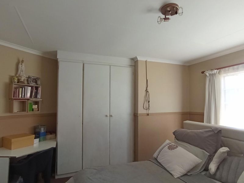 A bedroom featuring built-in cupboards, a dado rail, and a ceiling-mounted light fixture, offering a functional space with neutral wall tones.