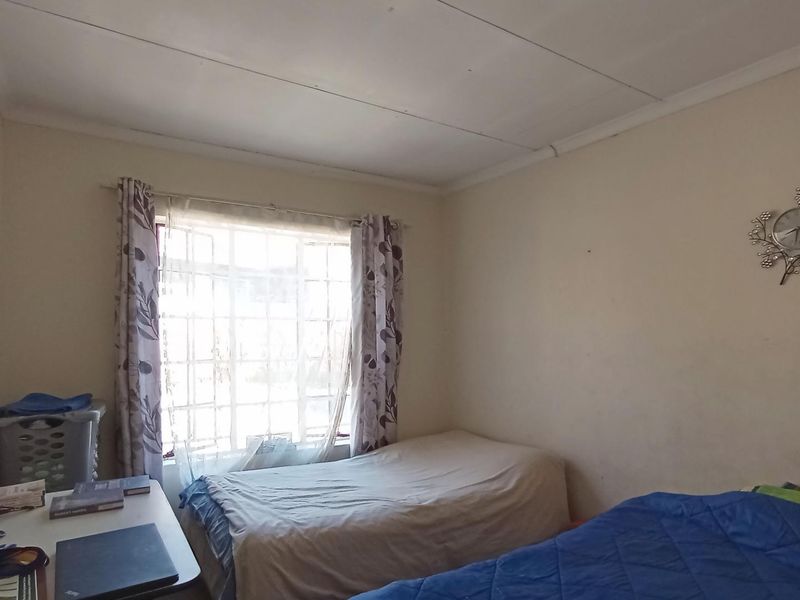 A functional bedroom featuring a window with security bars and standard ceiling tiles, requiring minor cosmetic updates to improve its overall appeal.