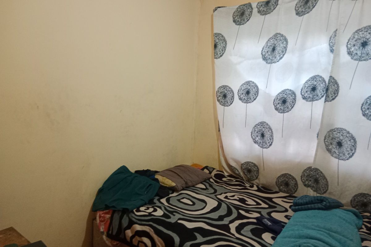 A compact bedroom featuring plain wall finishes and a window with patterned curtains, requiring cosmetic updates to improve the overall aesthetic.