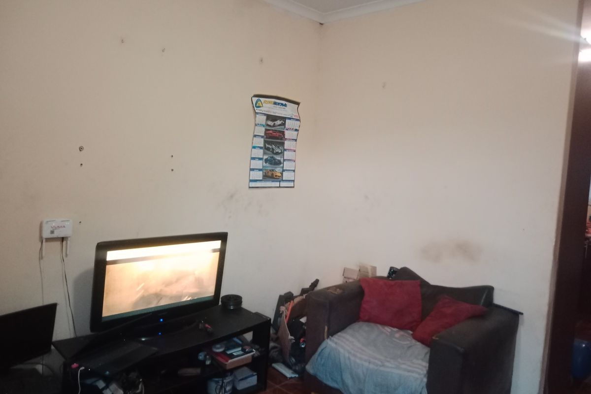 A living room area featuring tiled flooring and coving, currently showing signs of wear on the wall surfaces.