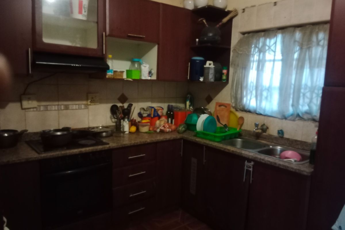 A dated kitchen featuring dark wood-look cabinetry, laminate countertops, a double bowl sink, and built-in cooking appliances with a tiled backsplash.