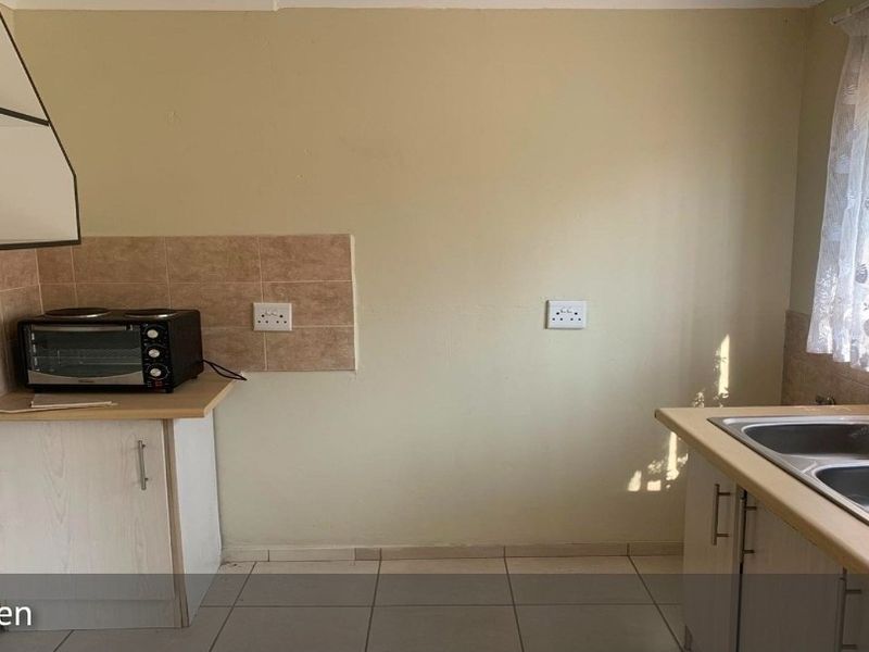 A functional kitchen featuring double bowl stainless steel sink, laminate countertops, base cabinetry, and tiled splashback with neutral wall finishes.