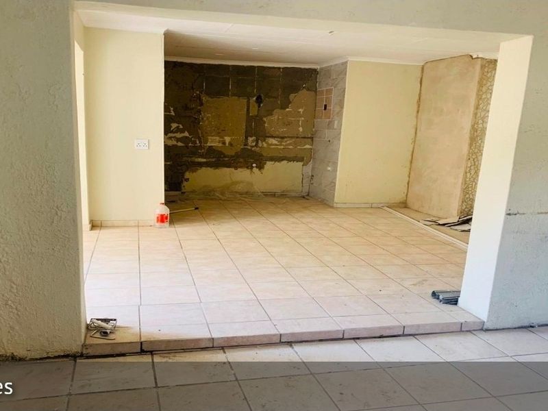 An empty, unfinished open-plan living area featuring tiled flooring and walls requiring plastering and finishing work.