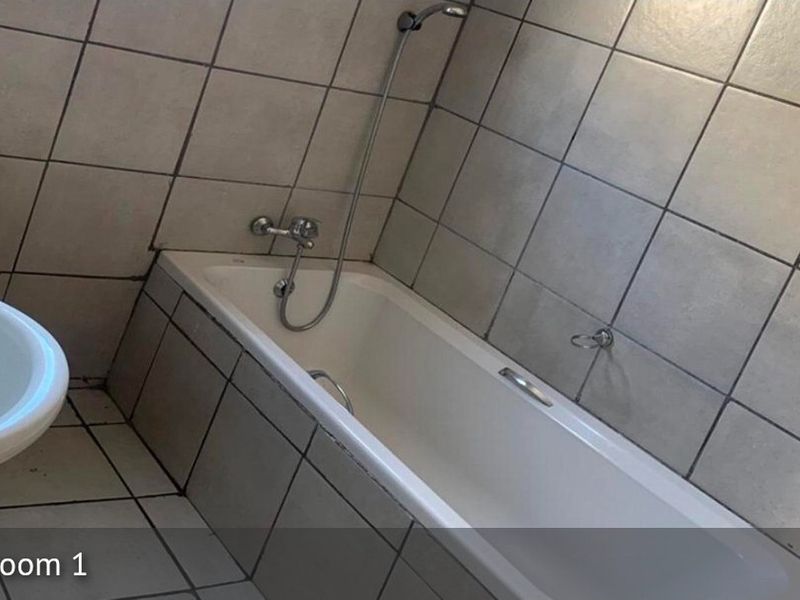 A functional bathroom featuring a standard bathtub with shower mixer, toilet, and full wall and floor tiling.