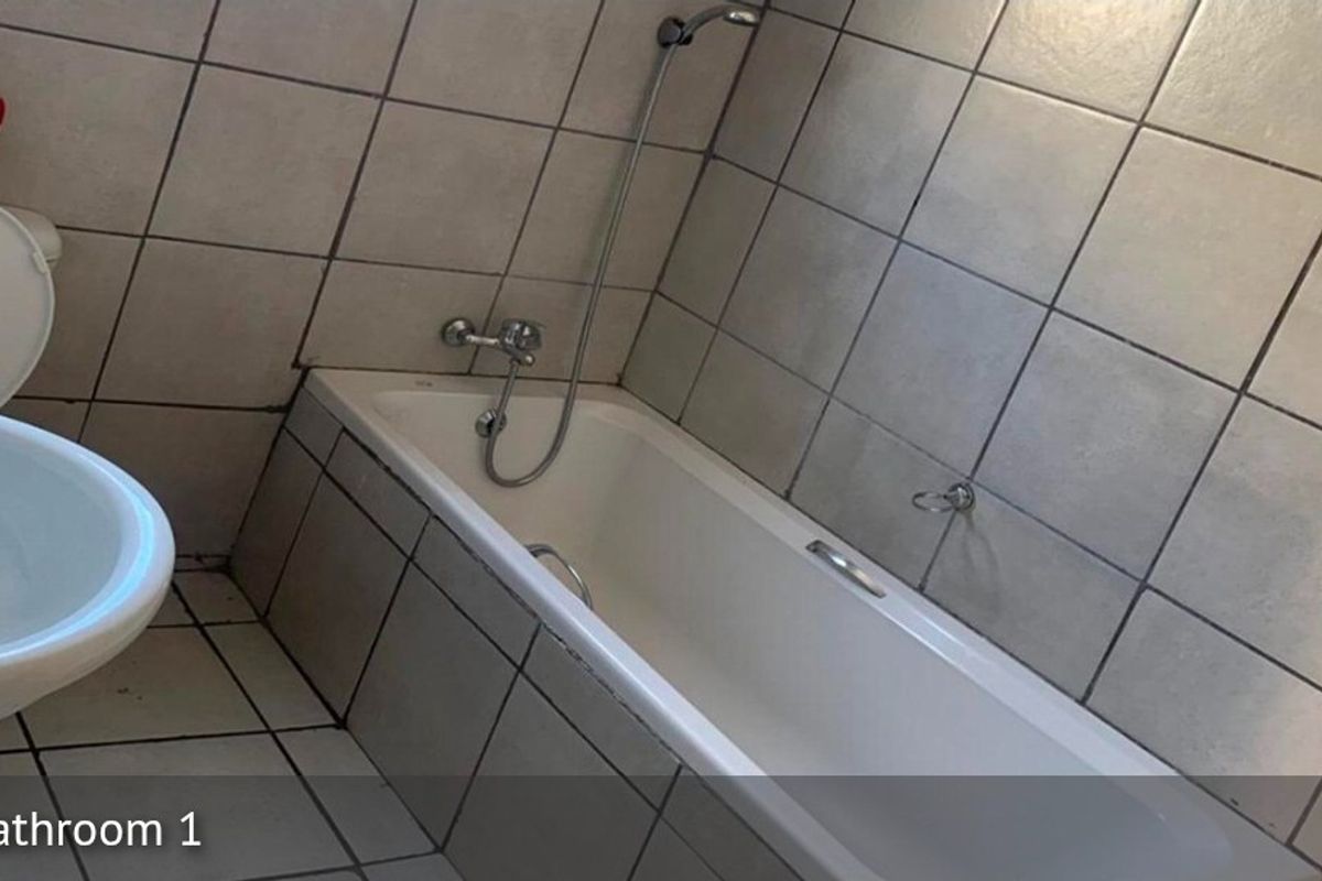 A functional bathroom featuring a standard bathtub with shower mixer, toilet, and full wall and floor tiling.