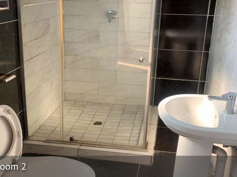 A functional bathroom featuring a glass-enclosed shower, pedestal basin, and toilet with contrasting black and white wall tiling.