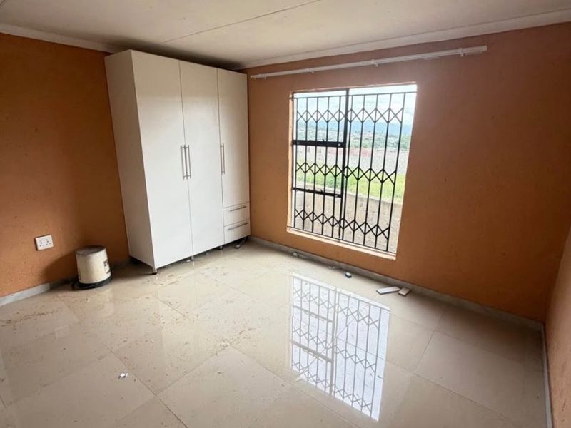 A vacant bedroom featuring tiled flooring, a built-in wardrobe, and a window fitted with a security gate.