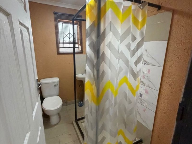 A compact bathroom featuring a pedestal basin, toilet, and a shower enclosure with tiled flooring and wall finishes.