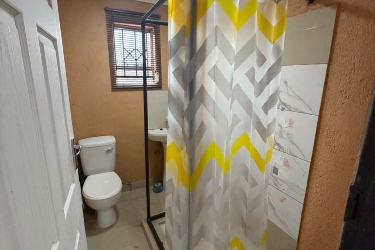 A compact bathroom featuring a pedestal basin, toilet, and a shower enclosure with tiled flooring and wall finishes.