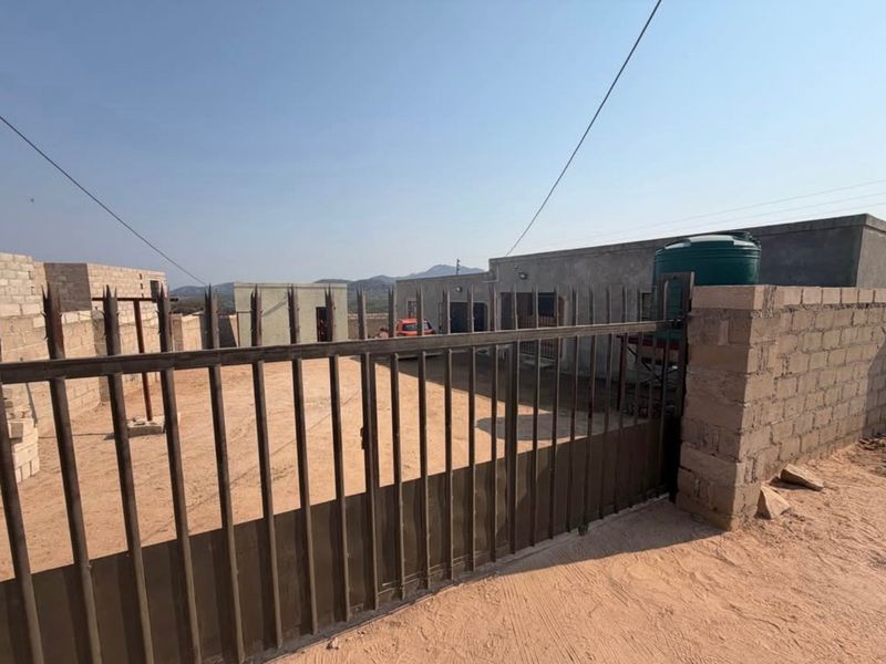 Front view of the property featuring a metal security gate, cinder block perimeter wall, and an external water storage tank.