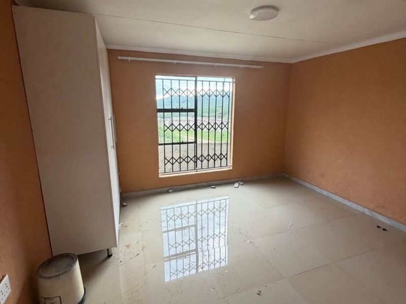 An empty bedroom featuring tiled flooring, a built-in wardrobe, and a window fitted with a security gate.