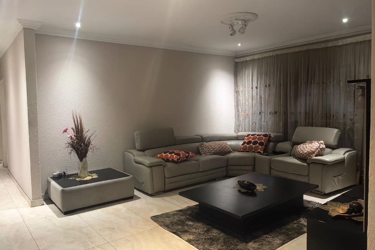 A well-maintained living room featuring neutral tiled flooring, recessed downlighting, and decorative ceiling coving, creating a comfortable and inviting space.