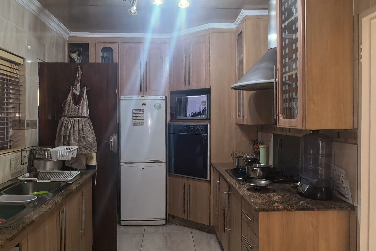 A functional kitchen featuring wood-finish cabinetry, granite countertops, built-in oven and microwave, stainless steel extractor fan, and tiled flooring.