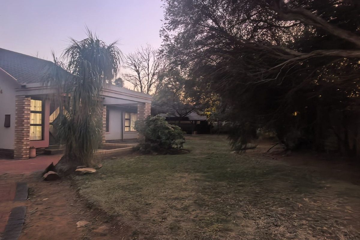 A view of the rear garden featuring a covered patio with brick pillars and a paved walkway at dusk.