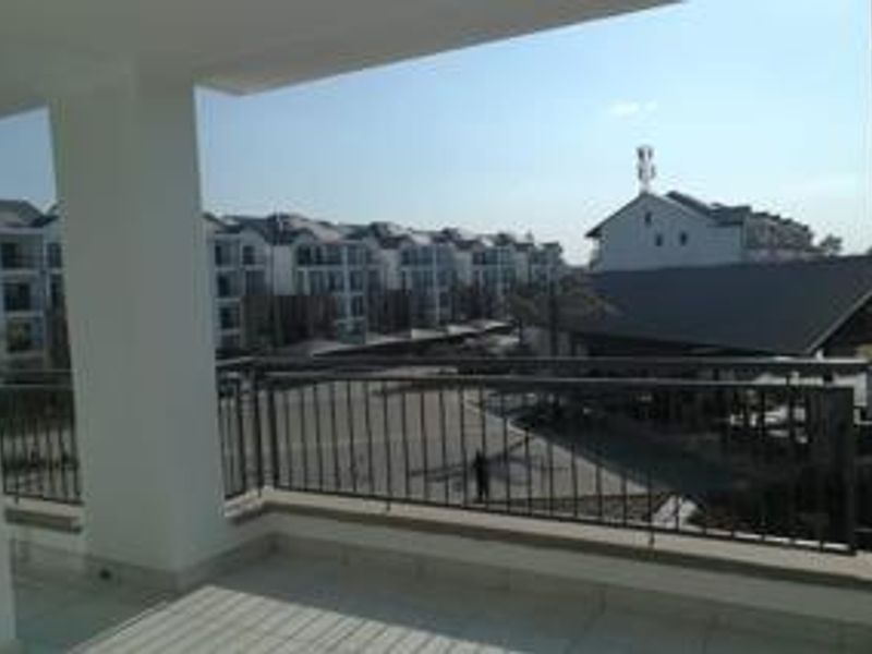A spacious covered balcony featuring tiled flooring and a metal balustrade, offering an elevated view of the surrounding apartment complex.
