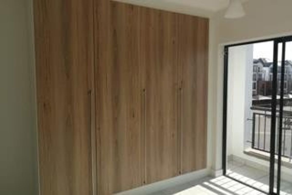 A bright bedroom featuring modern wood-finish built-in cupboards and a sliding glass door providing direct access to a private balcony.