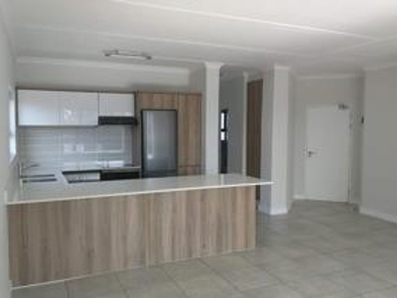 Modern open-plan kitchen featuring sleek cabinetry, stone countertops, and a functional island, seamlessly integrated into a spacious, tiled living area.