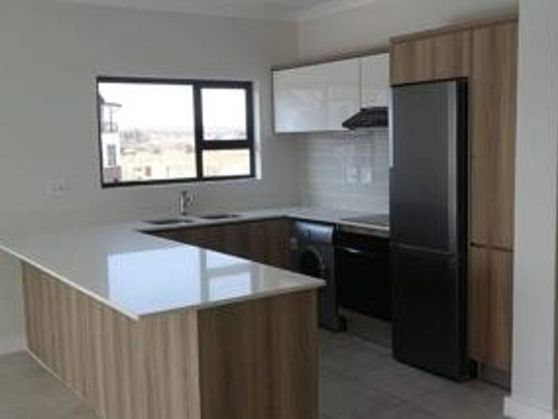 Modern kitchen featuring sleek wood-tone cabinetry, white quartz countertops, integrated appliances, and tiled flooring in a clean, contemporary open-plan layout.