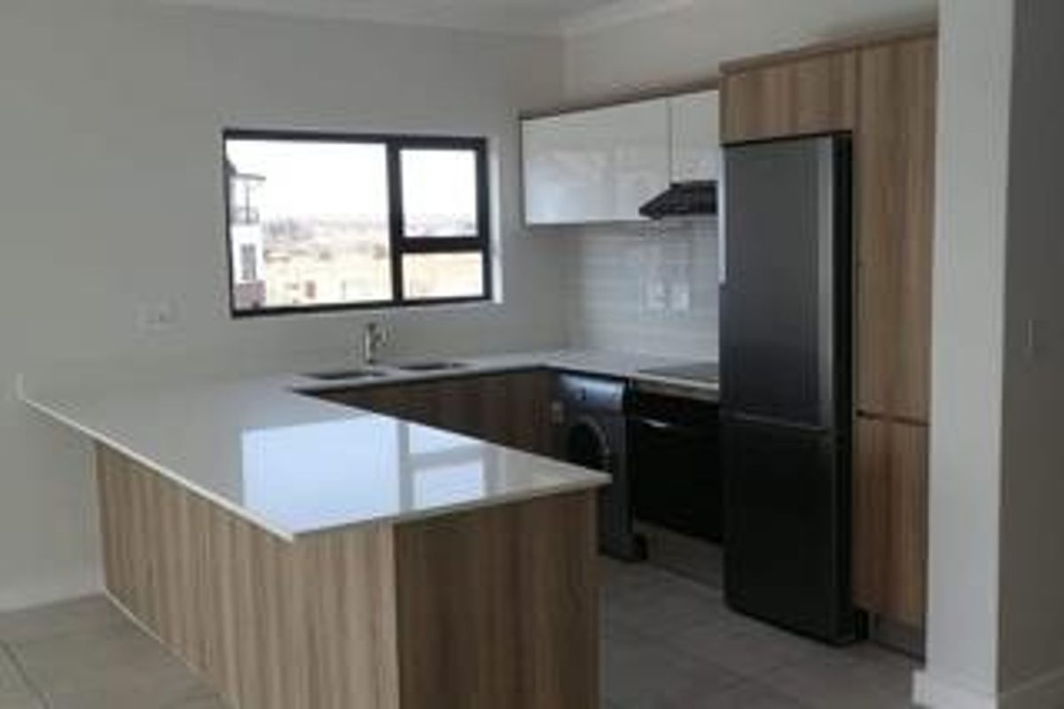 Modern kitchen featuring sleek wood-tone cabinetry, white quartz countertops, integrated appliances, and tiled flooring in a clean, contemporary open-plan layout.