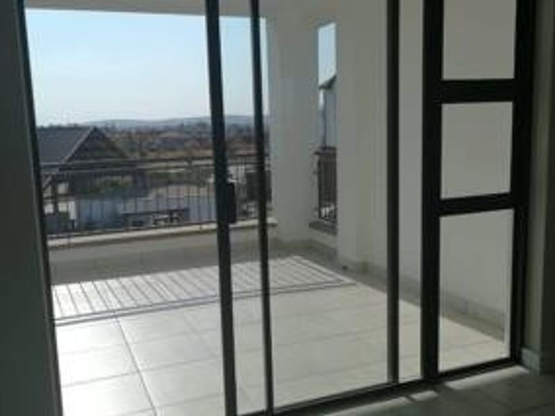 A spacious, tiled balcony featuring a metal balustrade and sliding glass door access, offering clear views of the surrounding area.
