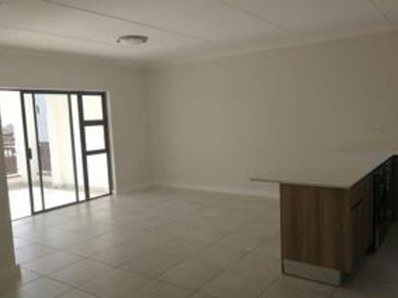 Spacious open-plan living area featuring tiled floors, a modern kitchen island with built-in cabinetry, and large sliding glass doors leading to a balcony.