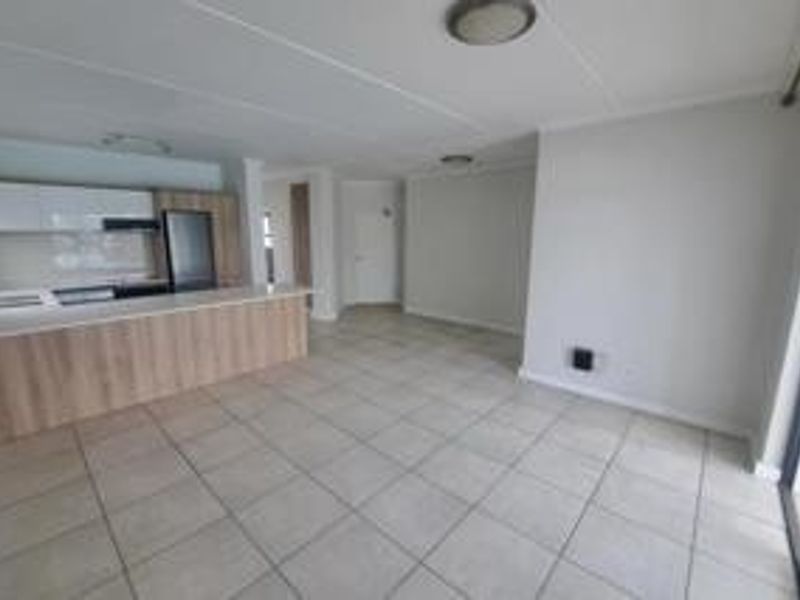 Spacious open-plan living area featuring a modern kitchen with a breakfast island, neutral tiled flooring, and direct access to an outdoor space.