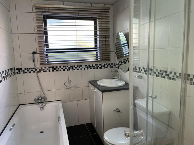 A functional bathroom featuring a bathtub, separate shower enclosure, vanity cabinet with basin, and tiled finishes throughout.