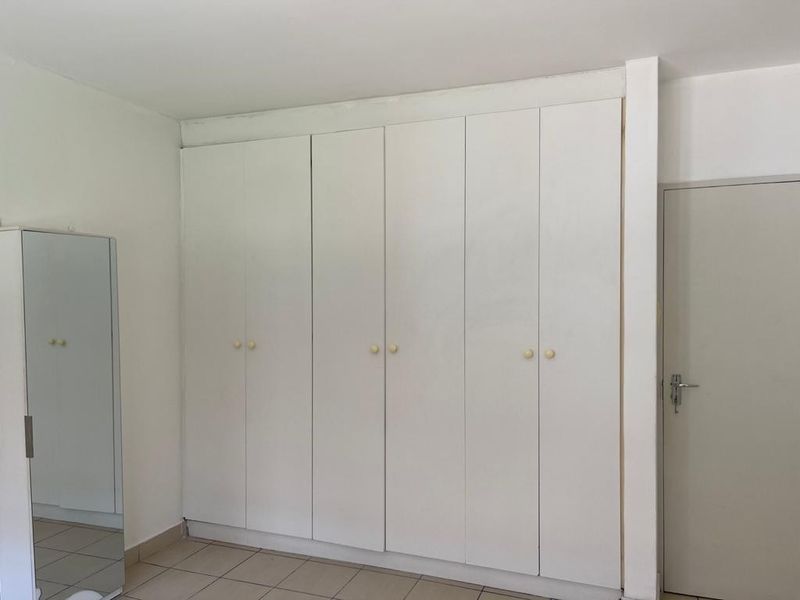 A bedroom featuring white built-in cupboards and tiled flooring, offering a clean and neutral space ready for personalization.