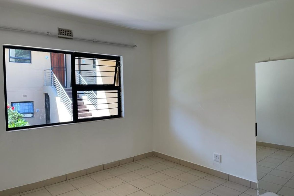 A simple, empty bedroom featuring tiled flooring, a window with security bars, and neutral walls, offering a blank canvas for personalization.