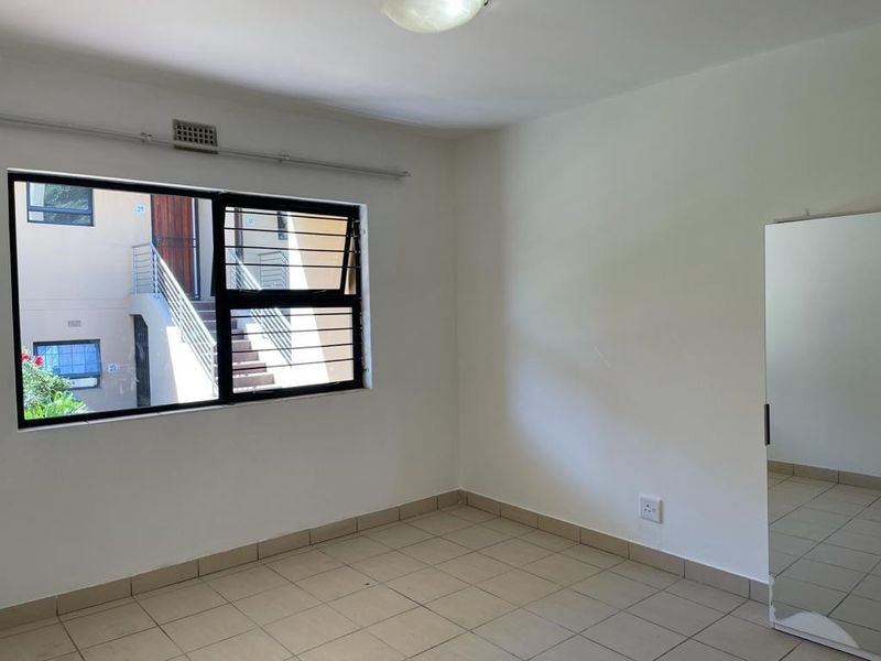 A simple, empty bedroom featuring tiled flooring, a window with security bars, and neutral walls, offering a blank canvas for personalization.
