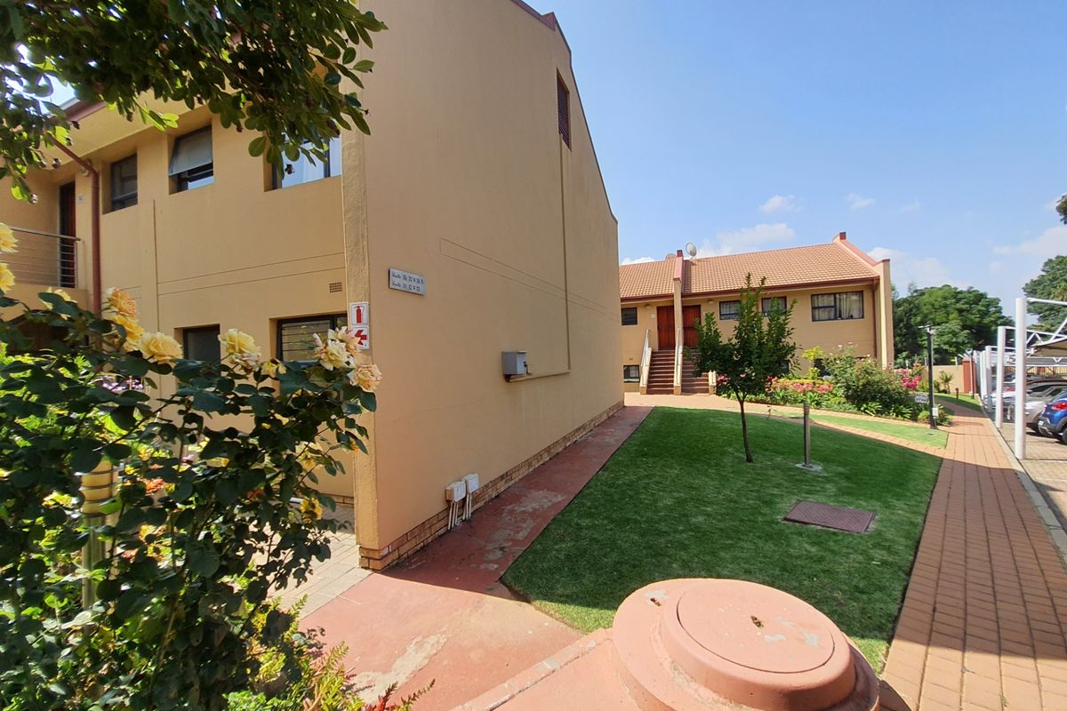 Exterior view of the townhouse complex featuring a paved walkway, landscaped lawn, and multi-story residential units with tiled roofing.