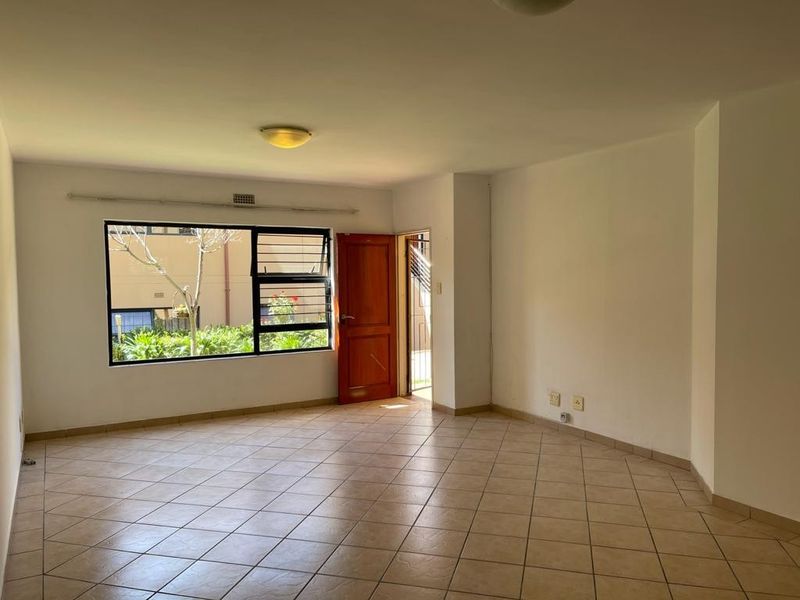 A spacious, empty living area featuring neutral tiled flooring, large windows providing natural light, and direct access to an outdoor space.