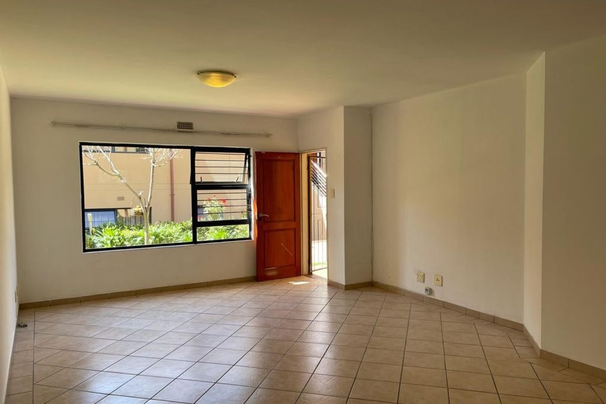 A spacious, empty living area featuring neutral tiled flooring, large windows providing natural light, and direct access to an outdoor space.