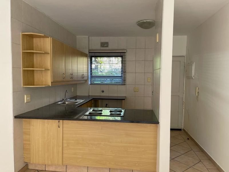 A functional kitchen featuring laminate cabinetry, granite countertops, and a built-in electric hob, offering a clean, blank canvas for potential modern updates.