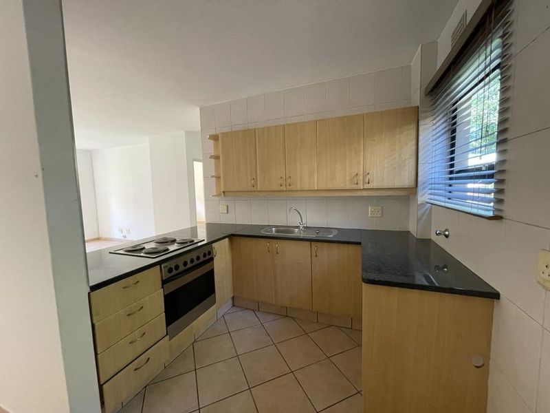 A functional kitchen featuring laminate cabinetry, dark countertops, built-in oven and hob, and tiled flooring, offering a clean space ready for modern updates.