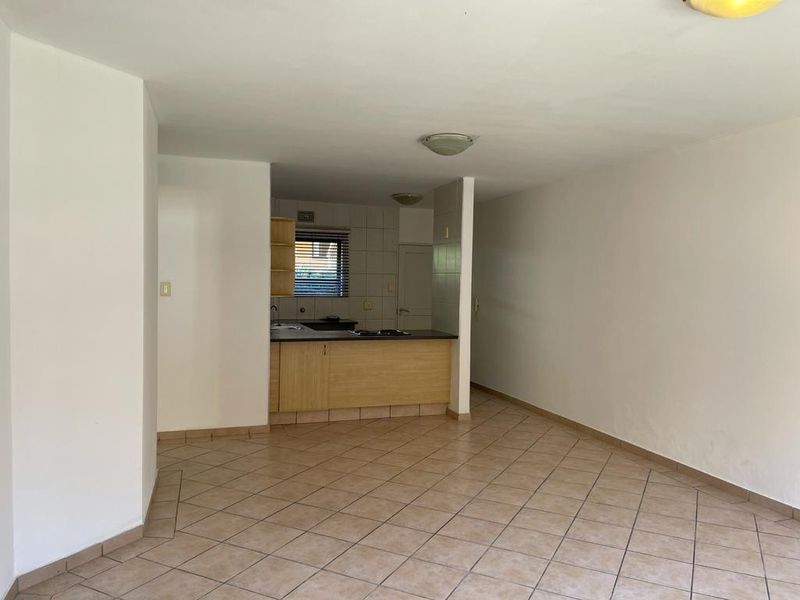 An open-plan living and kitchen area featuring tiled flooring, built-in cabinetry, and neutral walls, offering a blank canvas for potential renovation.