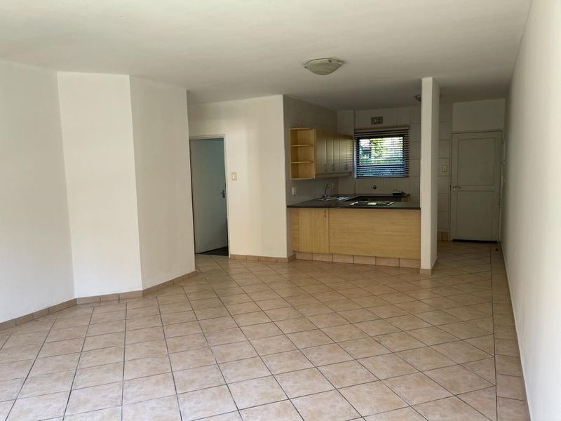 An open-plan living area featuring tiled flooring and a functional kitchen with built-in cabinetry, sink, and hob.