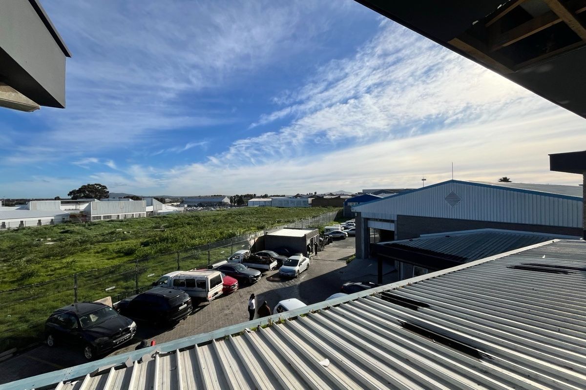 Elevated view of an industrial property featuring corrugated metal roofing, a paved parking area, and surrounding chain link fencing.
