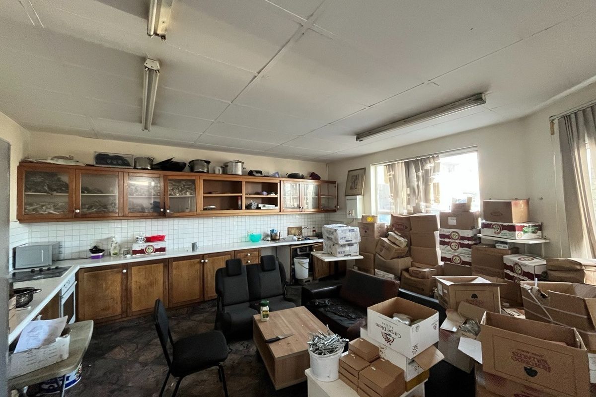A dated industrial kitchen space featuring extensive wooden cabinetry, tiled backsplash, and fluorescent lighting, currently used for storage.