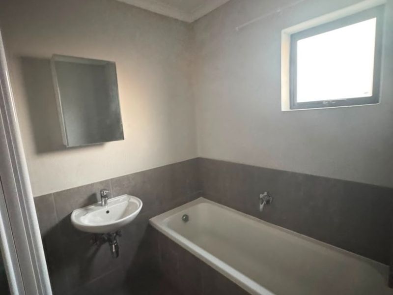 A functional bathroom featuring a built-in bathtub, wall-mounted basin, and neutral tiled finishes, offering a clean and simple layout.