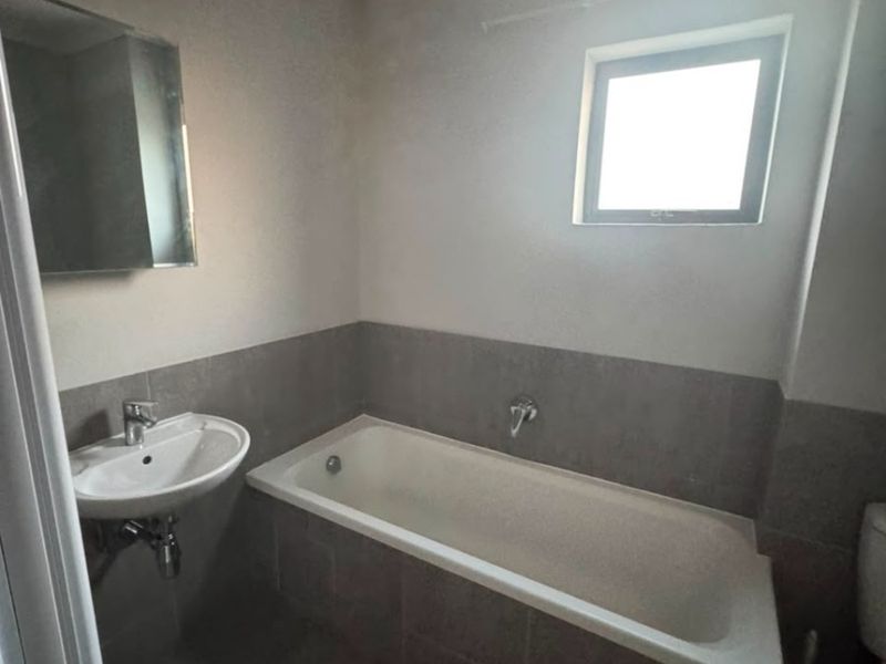A functional bathroom featuring a built-in bathtub, wall-mounted basin, and neutral tiled finishes, offering a clean and simple layout.