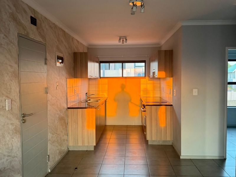 A clean, functional kitchen featuring wood-finish cabinetry, tiled flooring, and a tiled backsplash, offering a neutral space ready for personalization.
