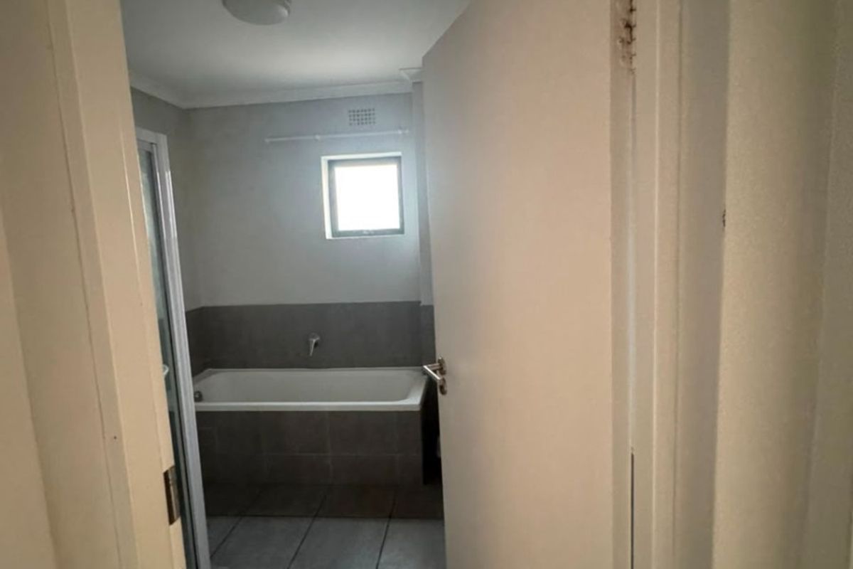 A functional bathroom featuring a bathtub, shower enclosure, and neutral tiled finishes, viewed from the doorway.