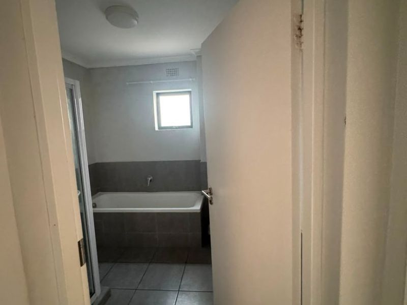 A functional bathroom featuring a bathtub, shower enclosure, and neutral tiled finishes, viewed from the doorway.