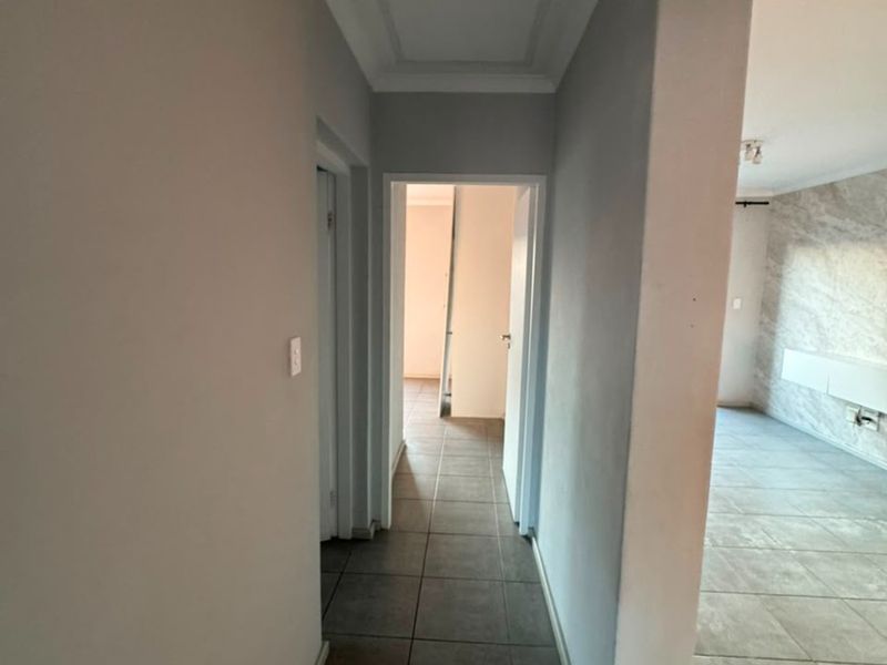 A clean, neutral-toned hallway featuring tiled flooring and a ceiling access hatch, providing a seamless transition between the living area and other rooms.
