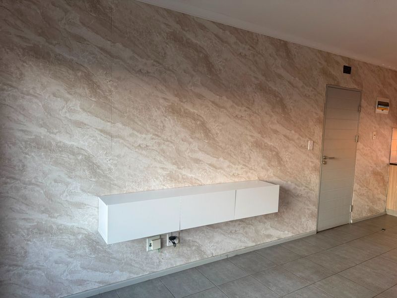 A living area featuring a feature wall with marble-effect finish, wall-mounted white cabinetry, and neutral tiled flooring.
