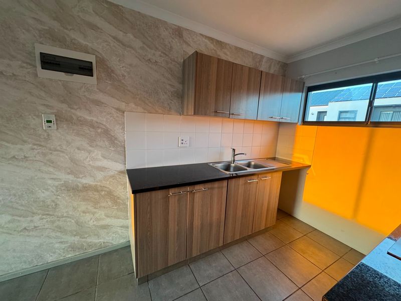 A clean, functional kitchen area featuring wood-look cabinetry, dark stone countertops, a stainless steel sink, and neutral tiled flooring.