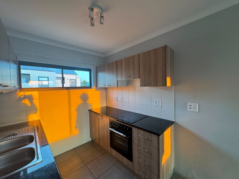 A functional kitchen featuring wood-finish cabinetry, granite countertops, a built-in electric oven and hob, and tiled splashbacks.