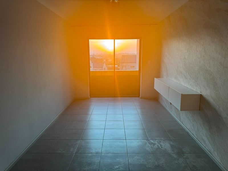 An empty living room featuring tiled flooring, wall-mounted storage, and a sliding glass door leading to a balcony with sunset views.